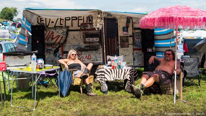 Wacken Open Air, man and woman sitting in padded chairs outside in front of a motorhome, with table and parasol Wacken Open Air, man and woman sitting in padded chairs outside in front of a motorhome, with table and parasol
