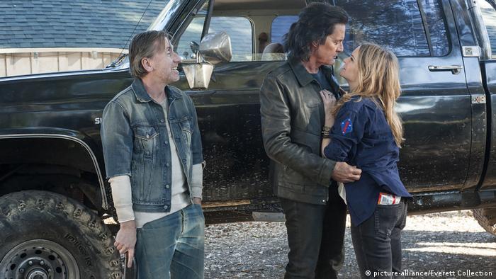 Film still from 'Twin Peaks' - three people in front of a pick-up truck: a man and a woman embrace while a third smiles in their direction.