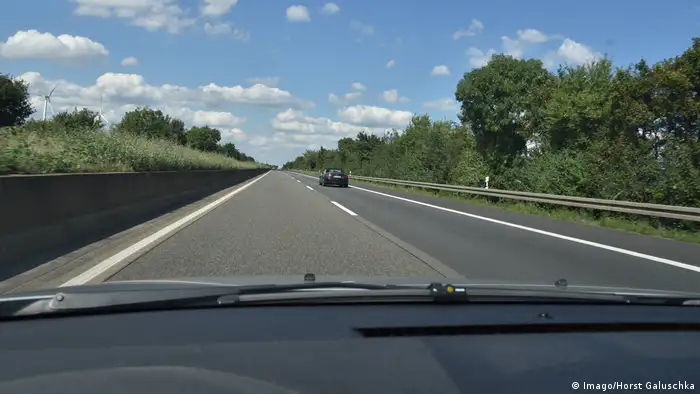 View through a windshield out onto the Autobahn with car in right lane. 