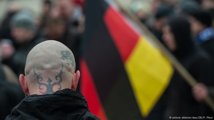 Ein rechter Lederkopf mit deutscher Flagge im Hintergrund während der Parade 2015