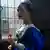 Filmstill aus "Tulpenfieber" (2017): Spohia (Alicia Vikander) steht im blauen Reneissance-Kleid am Fenster und hält eine gelb-rote Tulpe in der Hand