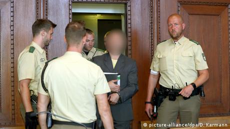 Wolfgang P., shown with face blurred, is escorted by guards in a Nuremberg courtroom 