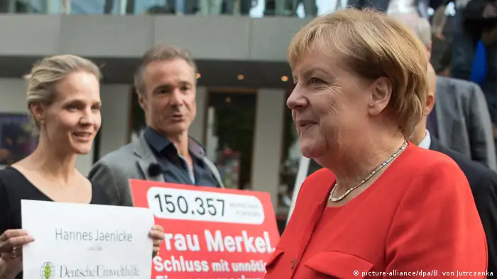 Hannes Jaenicke und Angela Merkel. Protest gegen Verpackungsmüll. (picture-alliance/dpa/B. von Jutrczenka)