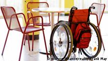 Ein Rollstuhl steht in der Kantine einer Schule am Tisch zwischen anderen Stühlen. | Verwendung weltweit