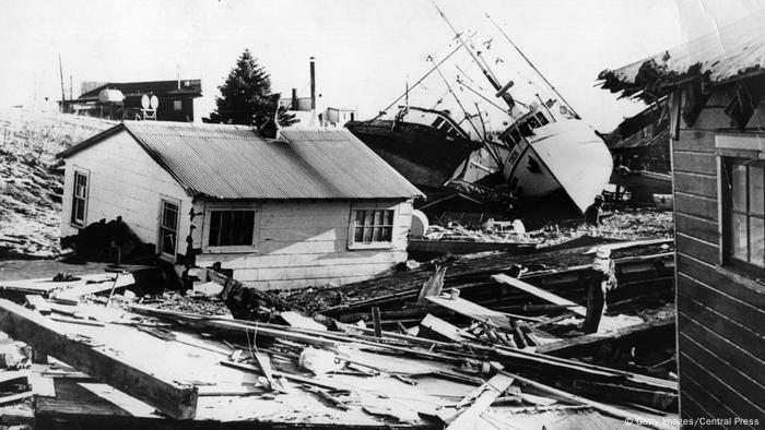 Schwarzweißaufnahme eines Fischerdorfs mit herumliegendem Schutt, zerstörten Häusern und aufgelaufenen Booten - nach dem Erdbeben in Alaska 1964