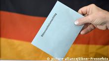ARCHIV *** Symbolbild Bundestagswahl, Hand steckt Stimmzettel im Stimmzettelumschlag in Wahlurne vor Deutschlandflagge | Verwendung weltweit