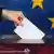 Hand steckt Stimmzettel in Wahlurne vor Europa-Flagge (Foto: Europäisches Parlament)