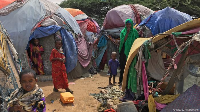 Children and a woman stand amongst makeshift tents held together by pieces of cloth (DW/S. Petersmann)