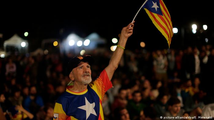 A man dressed in a shirt based on the Catalan flag hold a Catalan flag