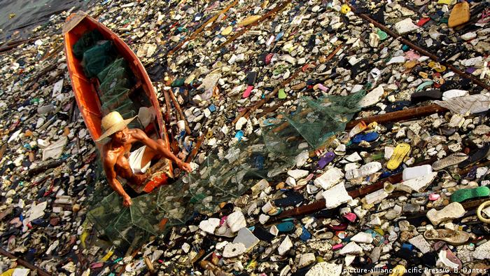 A fisherman in the Philippines removes a fish and crab trap from plastic-filled waters.