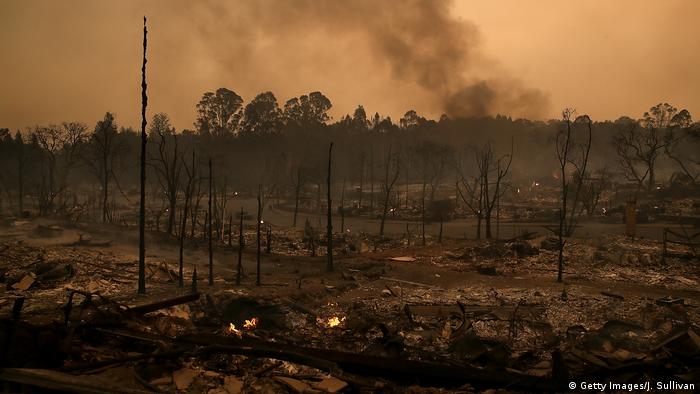 Smoke billows from a neighborhood that was destroyed by a fast moving wild fire