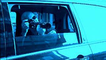 Ein Mann fotografiert mit einem langen Teleobjektiv aus einem Auto (Foto: DW TV)