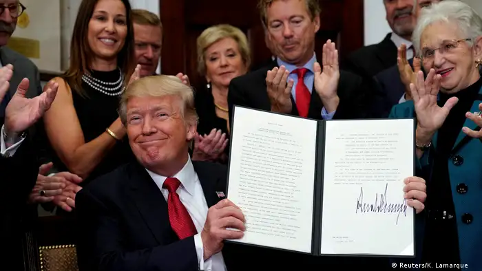 Trump smirks as he holds up a folder with plans for a bare-bones insurance offerings 