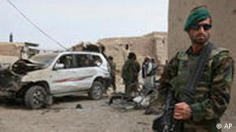 An Afghan soldier, right, stands guard as the damaged vehicle is seen at the site of a blast in Kandahar province