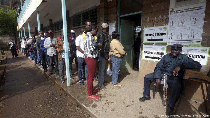 An armed policeman guards as people line up at a polling station before casting their vote in Nairobi