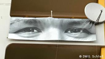 Man sieht ein Augenpaar, vergrößert auf einem Transparent, das am Balkon herunterhängt