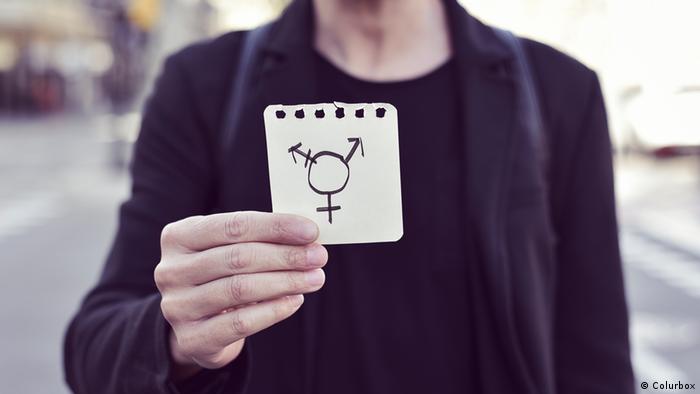 Foto de una persona con un papel con el logo trans en la mano.