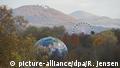 Eine Weltkugel und ein Riesenrad stehen am 13.11.2017 in Bonn (Nordrhein-Westfalen) am Rande der Weltklimakonferenz zwischen herbstlichen Blattwerk. Die Weltklimakonferenz COP23 findet 06. bis 17. November 2017 in Bonn statt. Im Hintergrund ist der Petersberg mit dem Hotel Petersberg zu sehen. Foto: Rainer Jensen/dpa | Verwendung weltweit