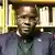 Nicholas Opiyo, Ugandan human rights activist, sitting in front of a bookshelf, wearing a navy blue blazer.