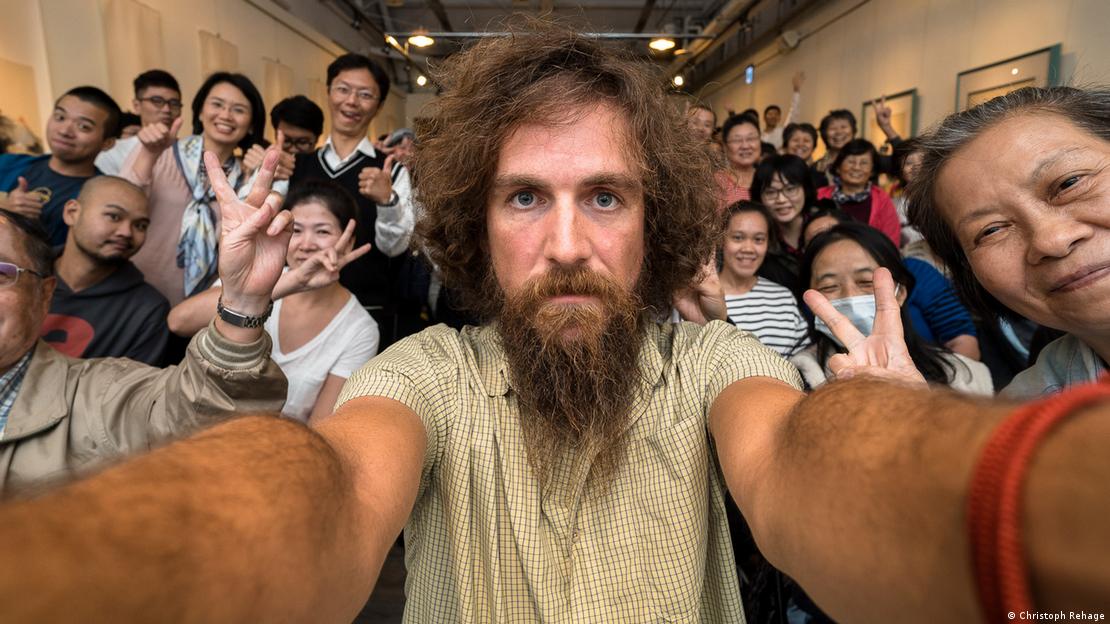 Christoph Rehage, a man with a long beard, takes a selfie among a large group of Chinese people.