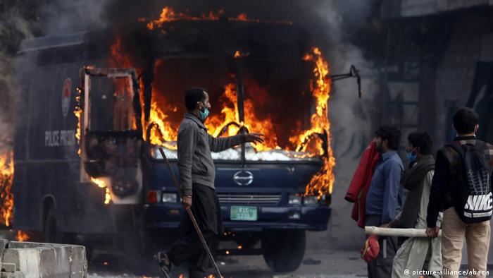 Pakistani protesters are seen beside a burning police van which was set on fire by them after security forces launched a crackdown.