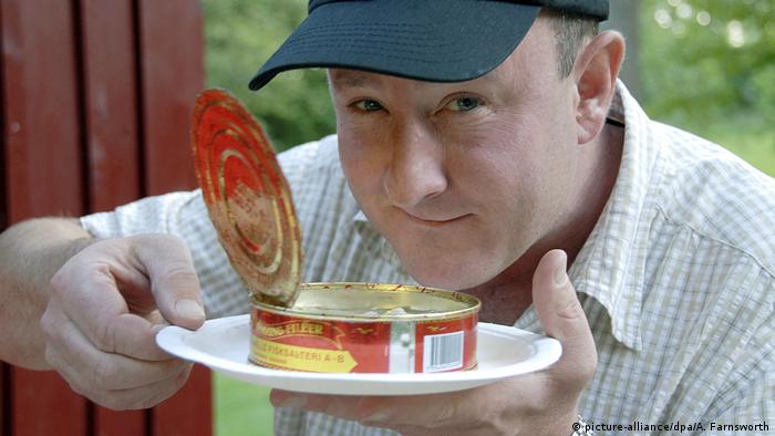 A can of the Swedish specialty Surströmming, or rotten fish, freshly opened by a smiling man and served on a plate (picture-alliance/dpa/A. Farnsworth)
