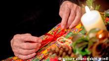 Hände eines Senioren öffnen die Schleife eines Weihnachts-Geschenks. | Verwendung weltweit