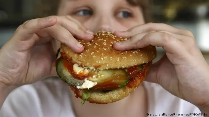 Kind hält Burger in der Hand (picture-alliance/Photoshot/PYMCA/N. Bo)