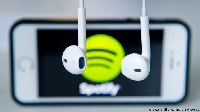Zwei Kopfhörer vor einem Smartphone, das das Spotify-Logo anzeigt. (picture-alliance/dpa/D.Bockwoldt)
