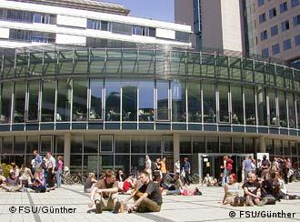 Students sit in front of a large university building's facade in downtown Jena