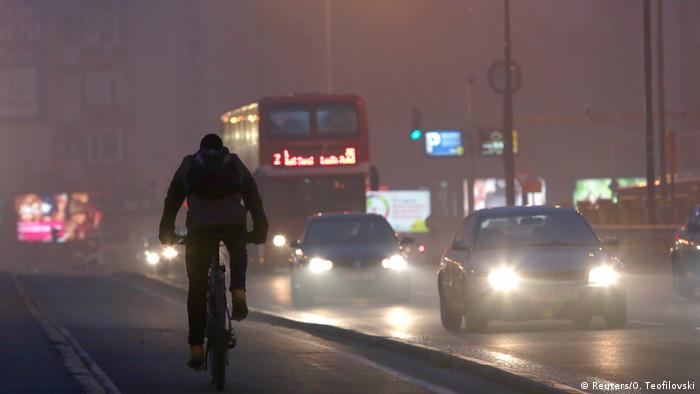 Vehicles and pedestrians are seen during evening fog and air pollution covering Skopje