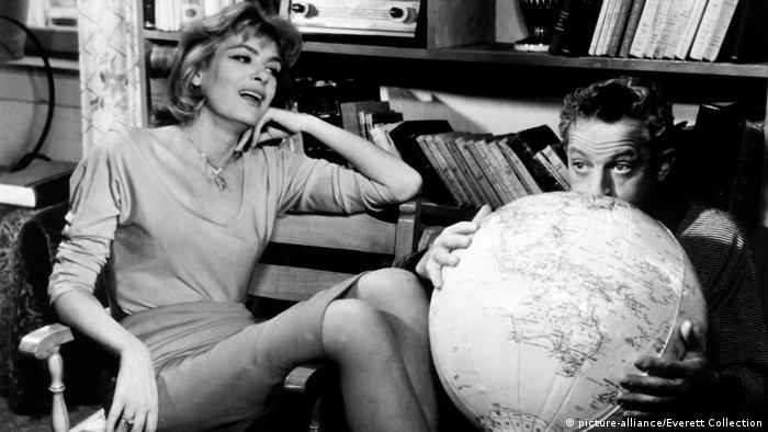 Melina Mercouri in Never on Sunday, film still. woman sits next to man blowing up a beachball with a planet earth design (picture-alliance/Everett Collection)