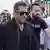 Salman Khan, wearing dark sunglasses, walks through a crowd of photographers.