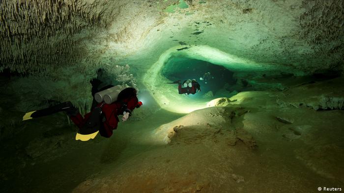 Divers with flashlights explore an underwater cavern