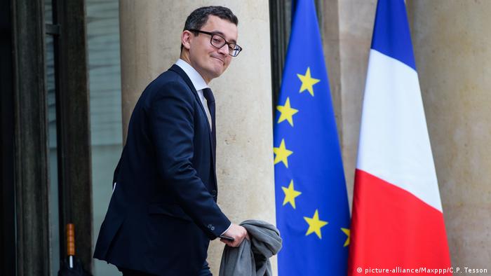 Gérald Darmanin walks next to an EU flag and a French flag