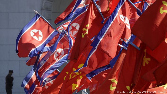 North Korean and Workers' Party flags flutter as a soldier walks by