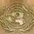 Emblema e Këshillit të Të Drejtave të Njeriut të OKB-së (kallinj gruri rrethojne globin prej rrathesh teli, me kontinentet mbi to)