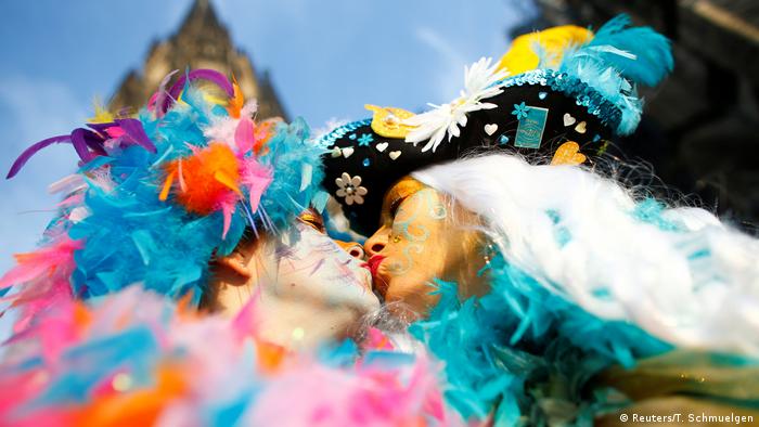 Two people kiss while wearing colorful feather boas. 