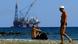A man walks as an other man sits on a beach as a drilling platform is seen in the background outside from Larnaca port, in the eastern Mediterranean island of Cyprus A man walks as an other man sits on a beach as a drilling platform is seen in the background outside from Larnaca port, in the eastern Mediterranean island of Cyprus