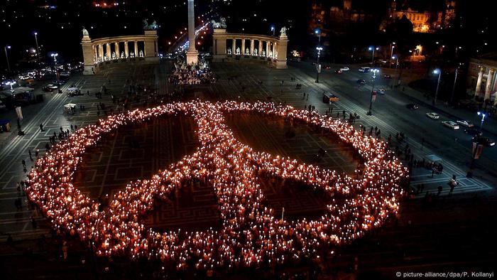 Anti-Kriegs-Demonstranten mit Fackeln formen ein Peace-Zeichen auf dem im Dunkeln liegenden Heldenplatz in Budapest. (picture-alliance/dpa/P. Kollanyi)