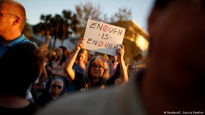 A woman holds a placard saying Enough is enough during a candlelight vigil for the victims of the shooting