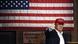 Donald Trump standing in front of a large American flag Donald Trump standing in front of a large American flag