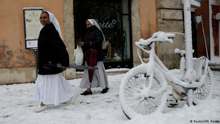 Nuns walk by snow covered bikes.