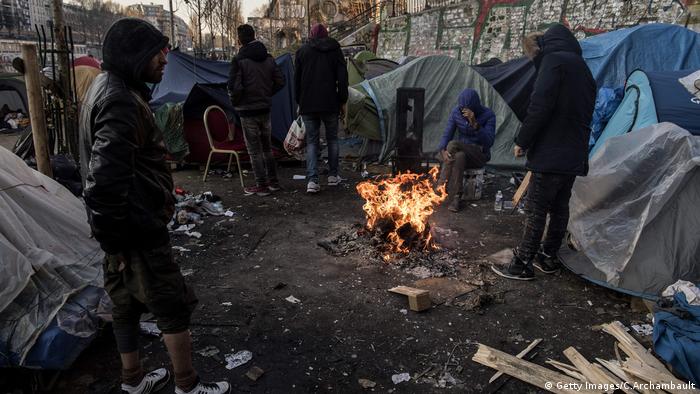 Migrants warm themselves around a bonfire in Paris, February 2018