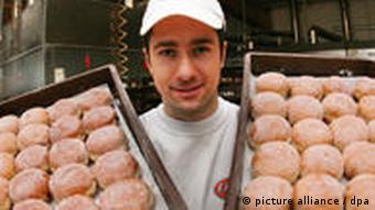 Ein Bäcker hält zwei Bleche mit Berliner Pfannkuchen hoch