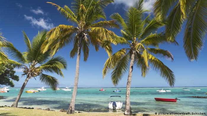 Mauritius Le Morne beach: Palmen am Strand und Motorboote dümpeln im türkisfarbenen Wasser