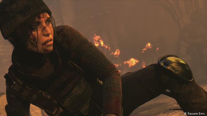 Screenshot Computerspiel Rise of the Tomb Raider, Lara Croft liegt verletzt am Boden, hinter ihr brennt es