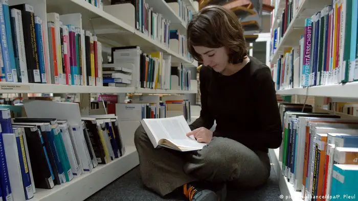 Ein Mädchen sitzt zwischen Bücherregalen und liest (picture-alliance/dpa/P. Pleul)