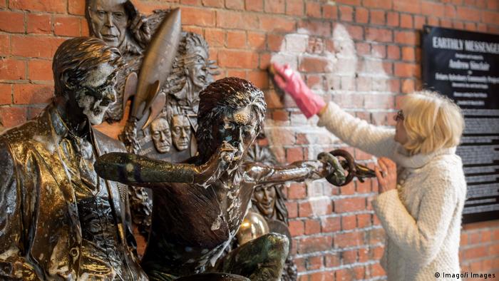 A woman removes graffiti from a wall next to a statue of David Bowie (Imago/i Images)