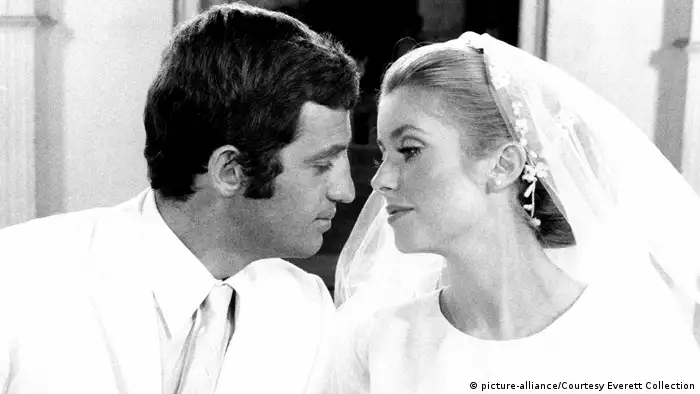 Jean-Paul Belmondo and Catherine Deneuve lean in to kiss one another